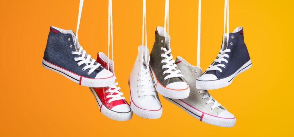 Stylish sneakers in various colors hanging with laces on a vivid orange backdrop. Ideal for fashion themes.